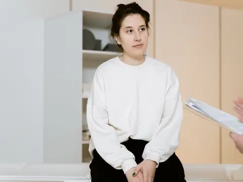 A woman in a white sweater listening during a consultation in a bright room