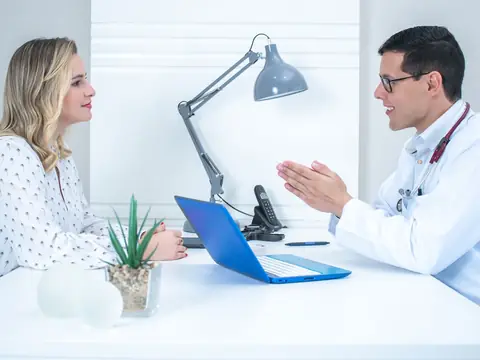 A woman talking with a doctor across a desk in a bright white office