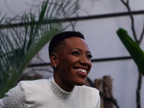 A smiling woman in a white sweater outdoors among green leaves