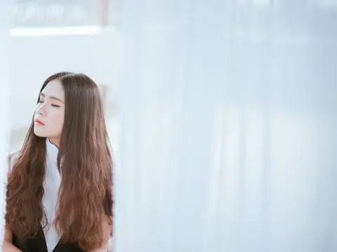 A woman with long hair resting quietly by a bright window