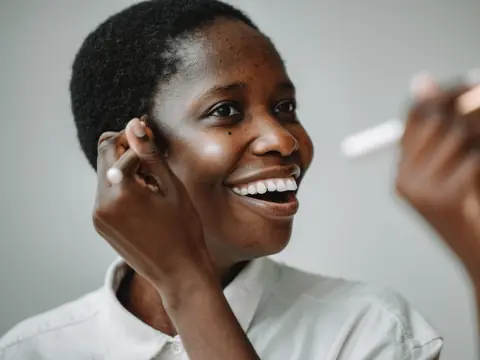 A woman laughing as she puts on makeup with a brush in a bright room